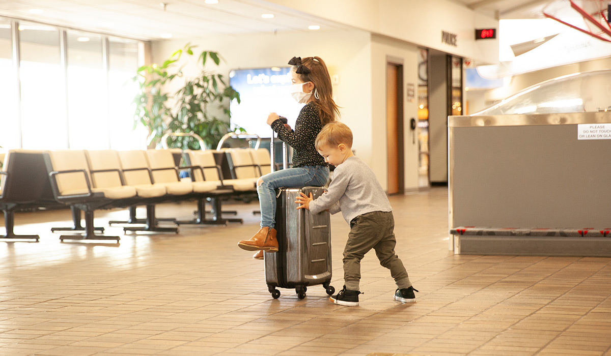 boy pushing girl on luggage through airport